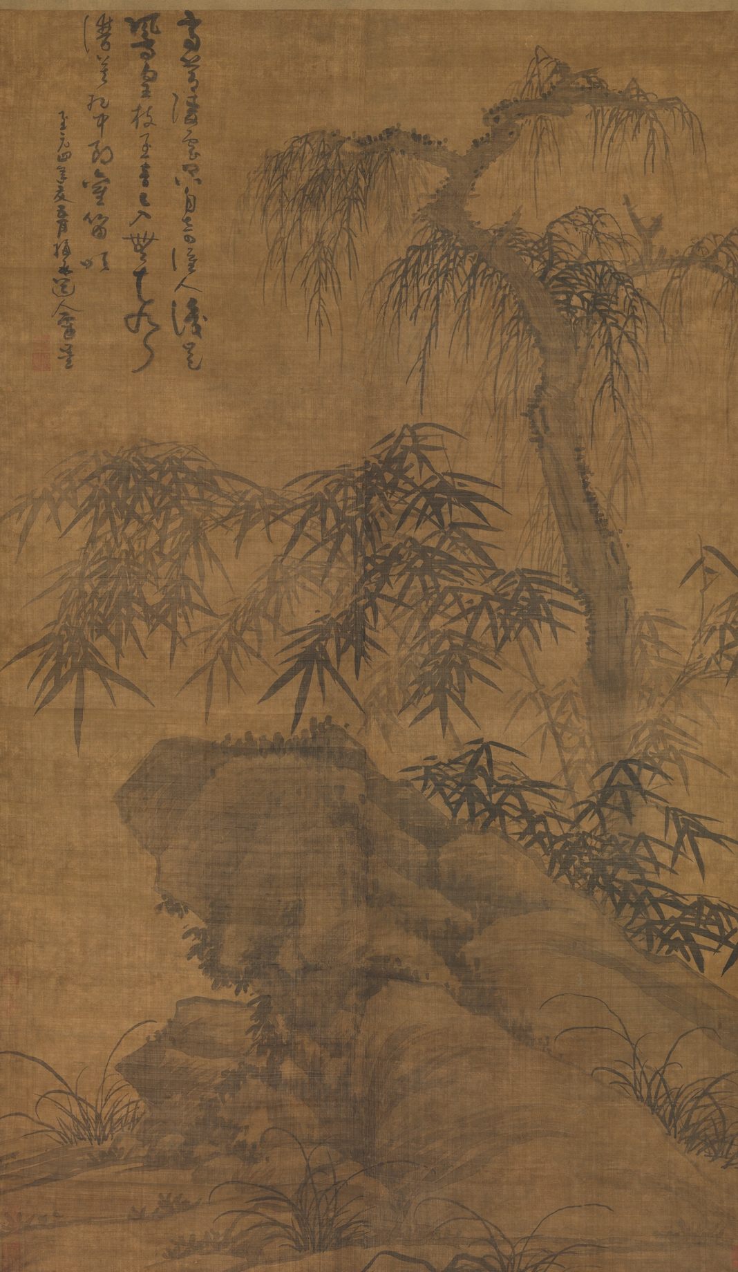 A tall ink painting on silk: slender bamboo springs up in supple leafed sprays beside a gnarled old tree leaning across the frame, with a large rounded rock below and tufts of grass at its foot. The artist's inscription is at the top left.
